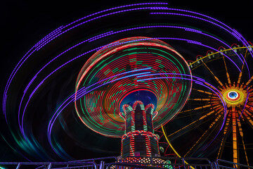Fun at the carousel ride at the late evening, colorful long exposure with light trails of the carousels rotation with a ferris wheel in the background.
