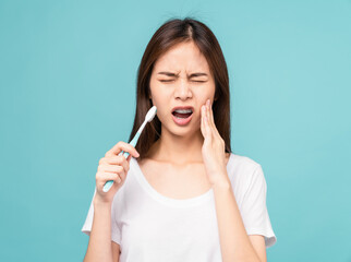 Asian woman wearing braces with brushing teeth with sensitive teeth on blue background, Concept...