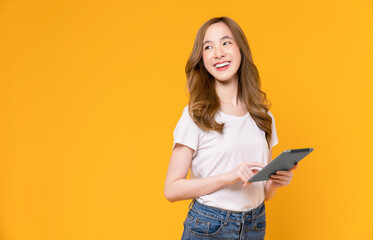 Young Asian woman holding digital tablet and smiling with touch on screen, light yellow background