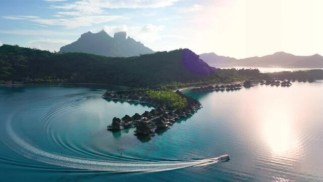 Luxury travel vacation aerial of overwater bungalows resort in coral reef lagoon ocean by beach. Aerial Drone video at sunset paradise getaway Bora Bora, French Polynesia, Tahiti, South Pacific Ocean.