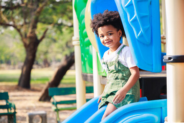 Fototapeta na wymiar Cute African American little kid boy funny while playing on the playground in the daytime in the spring season. Outdoor activity. Playing make-believe the concept. Outside education