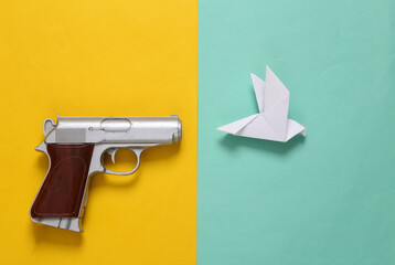 Creative layout of gun and origami dove on yellow blue background. Peace.No war. Top view