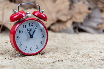 Red analog clock and maple leaves in the background