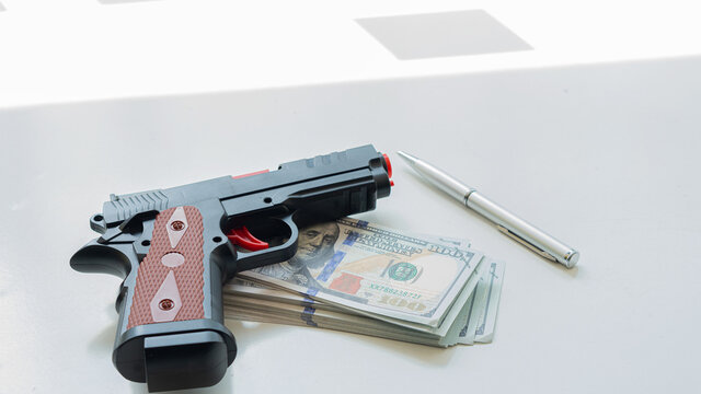 A gun and a dollar and a pen on the desk