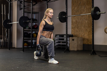 Fit woman in sportswear doing lunges with a kettlebells in her hands in gym. Functional training