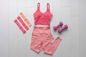 Fitness clothes flat lay workout at home with resistance bands and dumbbell weights. Pink athleisure fashion clothing top view on white wood floor. - 431419178