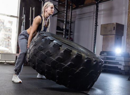 Fit female athlete flipping huge tire. Woman lifts a heavy wheel. Muscular young woman doing functional training exercise at gym.