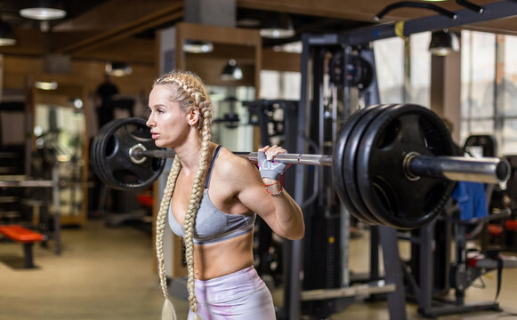 Fit woman with long pigtails, Athletic lady with heavy barbell on shoulders in gym