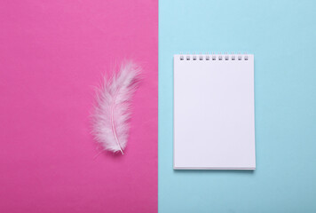 Feather and notebook on pink blue background. Minimalism. Top view. Flat lay