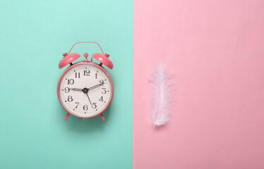 Soft feather and alarm clock on pink blue pastel background. Minimalism. Top view. Flat lay