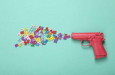 Pink pistol gun shooting colored letters on mint blue background. Creative minimalism layout....