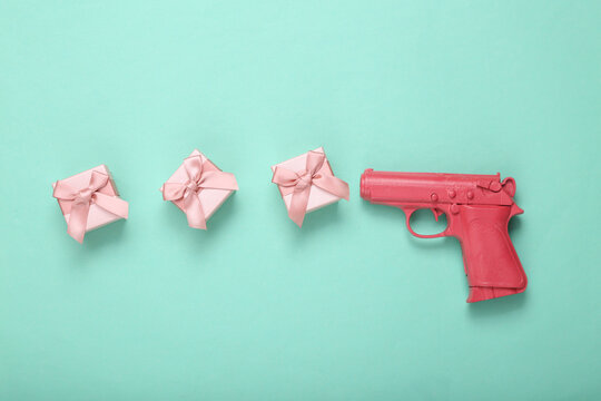 Pink pistol gun shooting gift boxes on mint blue background. Creative holiday layout. Flat lay. Top view