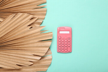 Creative layout. Pink calculator on blue background with dry palm leaves. Flat lay. Top view