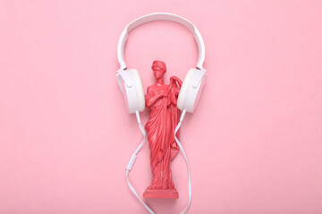 Creative layout. Pink Antique greek goddess statue with headphones on pink background. Flat lay. Top view