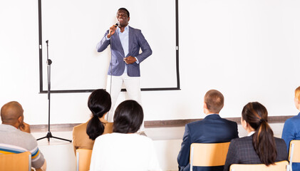 Young emotional male motivation coach giving speech from speaker stage