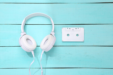 Music creative layout. White audio cassette and headphones on blue wooden background. Minimalism. Top view. Flat lay