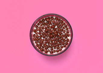 Chocolate cereal balls with milk in bowl on pink background. Concept for a healthy diet. Top view