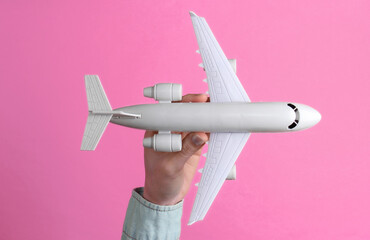 Female hand holds a toy airplane on pink background. Travel concept