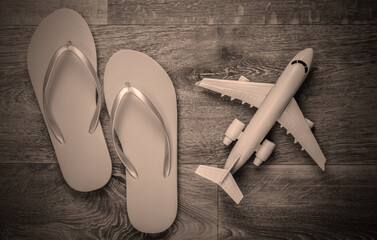 Travel flat lay composition. Plane figurine, flip flops on wooden floor. Beach vacation. Top view