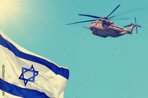 Israeli National flag waving and Military armed helicopter against blue sky.  Sun shining. Independence day concept
