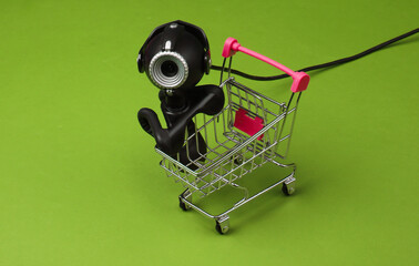 Shopping cart with web camera on green background.