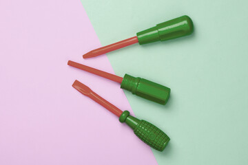 Set of plastic toy screwdrivers on pink green pastel background