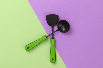 Toy kitchen tools on a pink-green pastel background. Kitchen spatula, ladle. Top view