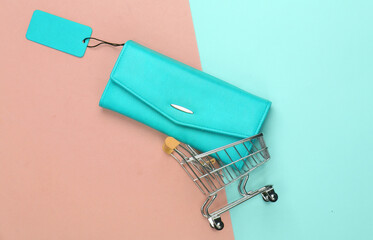 Shopping trolley and fashionable leather wallet with blue sale tag on colored background. Top view. Discount. Minimalism