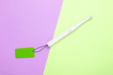 Fototapeta na wymiar Electro toothbrush with green sale tag on colored background. Big Sale, discounts. Top view
