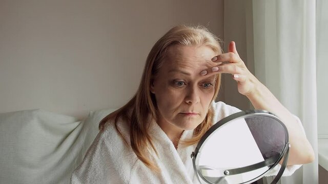 aging woman is surprised at her wrinkles on her forehead while looking in the mirror