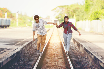 Young couple walking hand in hand on railway tracks, along railroad togethe