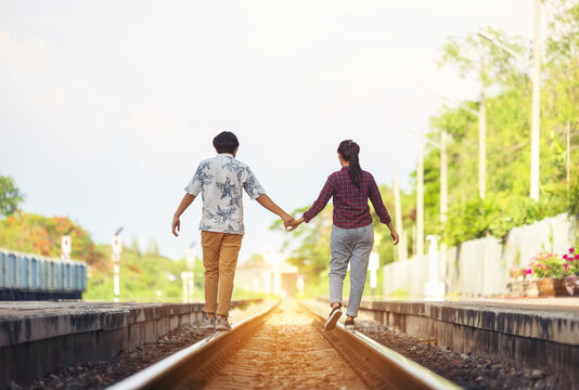 Young couple walking hand in hand on railway tracks, along railroad togethe