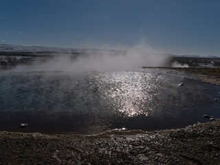 Steaming pool with hot thermal water in Geysir in geothermal area Haukadalur, part of Golden Circle, Iceland in winter season on sunny day with reflections.