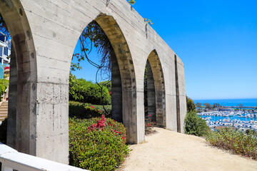 a gorgeous shot of 3 stone arches covered with lush green plants and red flowers with beautiful views of the deep blue ocean and blue sky at Dana Point Bluff Top Trail in Dana Point CA - obrazy, fototapety, plakaty