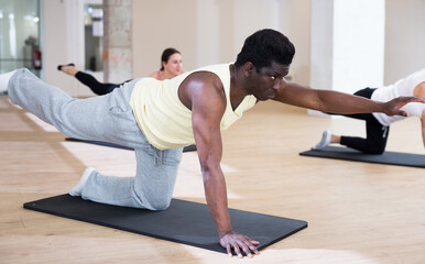 Fototapeta na wymiar Portrait of focused African American man performing set of pilates exercises with group in fitness studio