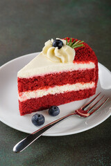 A slice of festive Red Velvet cake with blueberries on dark green background. Copy space.