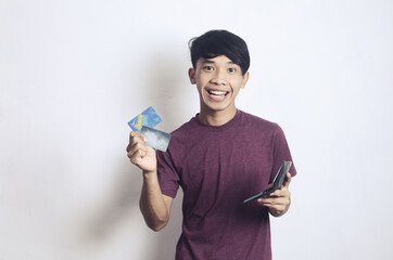 young Asian man with a cheerful expression carrying an ATM card and wallet on a white background