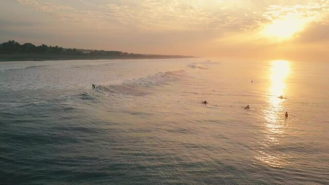 Surfer riding wave and people floating in ocean during orange sunset