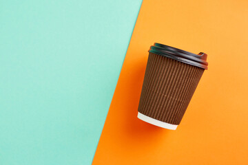 Paper coffee cup on orange and  turquoise background. Closeup blank craft paper coffee cup. Place for text.