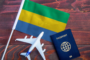 Flag of Gabon with passport and toy airplane on wooden background. Flight travel concept. 