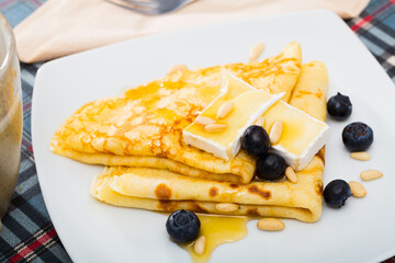 Sweet crepes served with soft creamy brie, berries of blueberry, roasted pine nuts and topped with honey