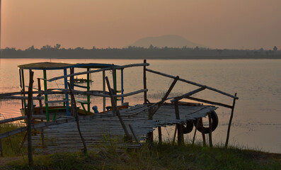 Fototapeta na wymiar a broken bridge leading to the lake and a boat captured during sunset.