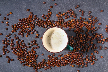Cup of coffee on a gray table with coffee beans and coffee leaves. Top view.