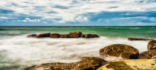Fototapeta na wymiar Smooth dramatic sea with rocks and a cloudy sky