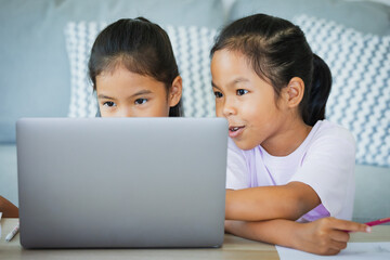 Two asian child girl students study online with teacher by video call together. Siblings are homeschooling with computer laptop during quarantine due to Covid 19 pandemic.