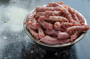 Raw chicken necks in a metal bowl on a black with white background.