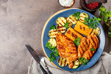 Grilled chicken breast with corn and zucchini on a blue plate top view. Summer dish with grilled chicken and vegetables. Photo with copy space for text