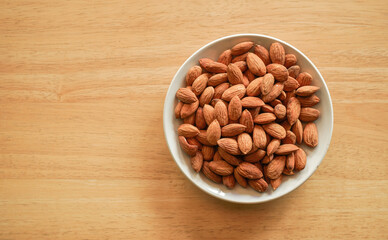 flat lay view of almond nuts in white dish on wood table with copy space