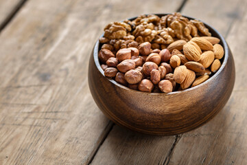 Nuts assortment - hazelnuts, walnuts and almonds in wooden bowl on wooden background close up, copy space