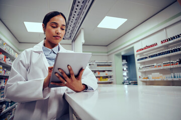 Low angle view of young female woman wearing labcoat working in chemist using digital tablet to confirm online order